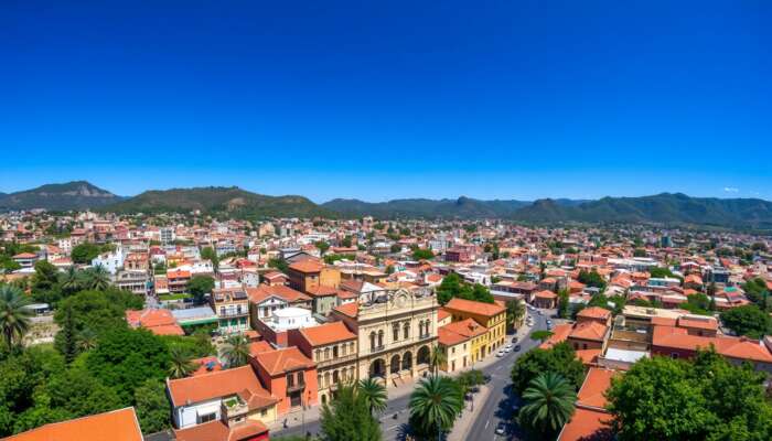 Aerial view of San Miguel de Allende featuring colorful colonial buildings, cobblestone streets, and green hills under a clear blue sky.
