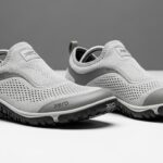 A pair of light gray slip-on athletic shoes with mesh uppers, rubber soles, and "Xero Shoes" branding offers all-day comfort and walking excellence, set against a plain gray and white background.